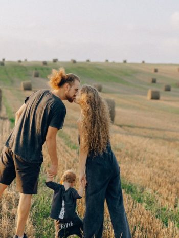 A couple with their child enjoy a sunny day in a wheat field, symbolizing love and joy.