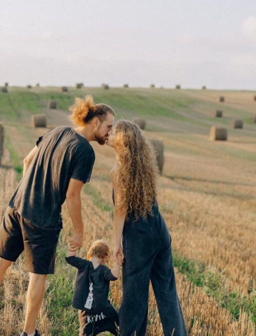 A couple with their child enjoy a sunny day in a wheat field, symbolizing love and joy.