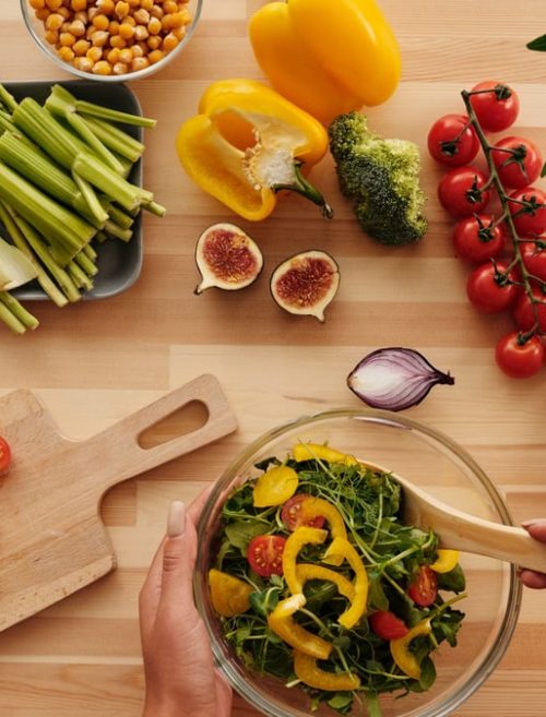Top view of fresh vegetables and salad preparation on a wooden table, perfect for healthy eating concepts.